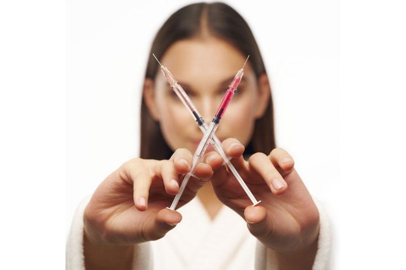 woman who is a botox specialist holding two syringes for facial fillers