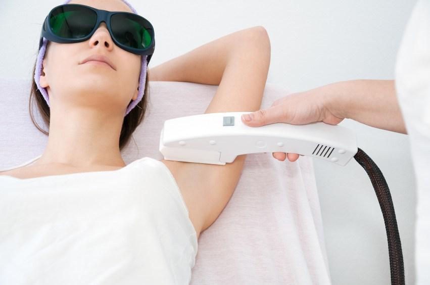 young woman wearing goggles and doctor applying laser hair removal procedure